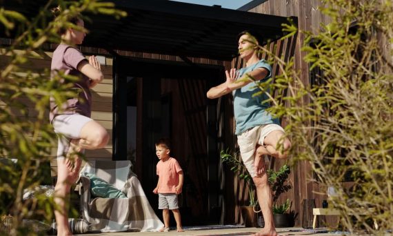 A family practicing yoga in tree pose on a sunlit porch, promoting health and mindfulness.