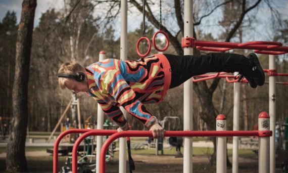 Young adult man exercises on outdoor gym bars in a colorful outfit in Vilnius, Lithuania.